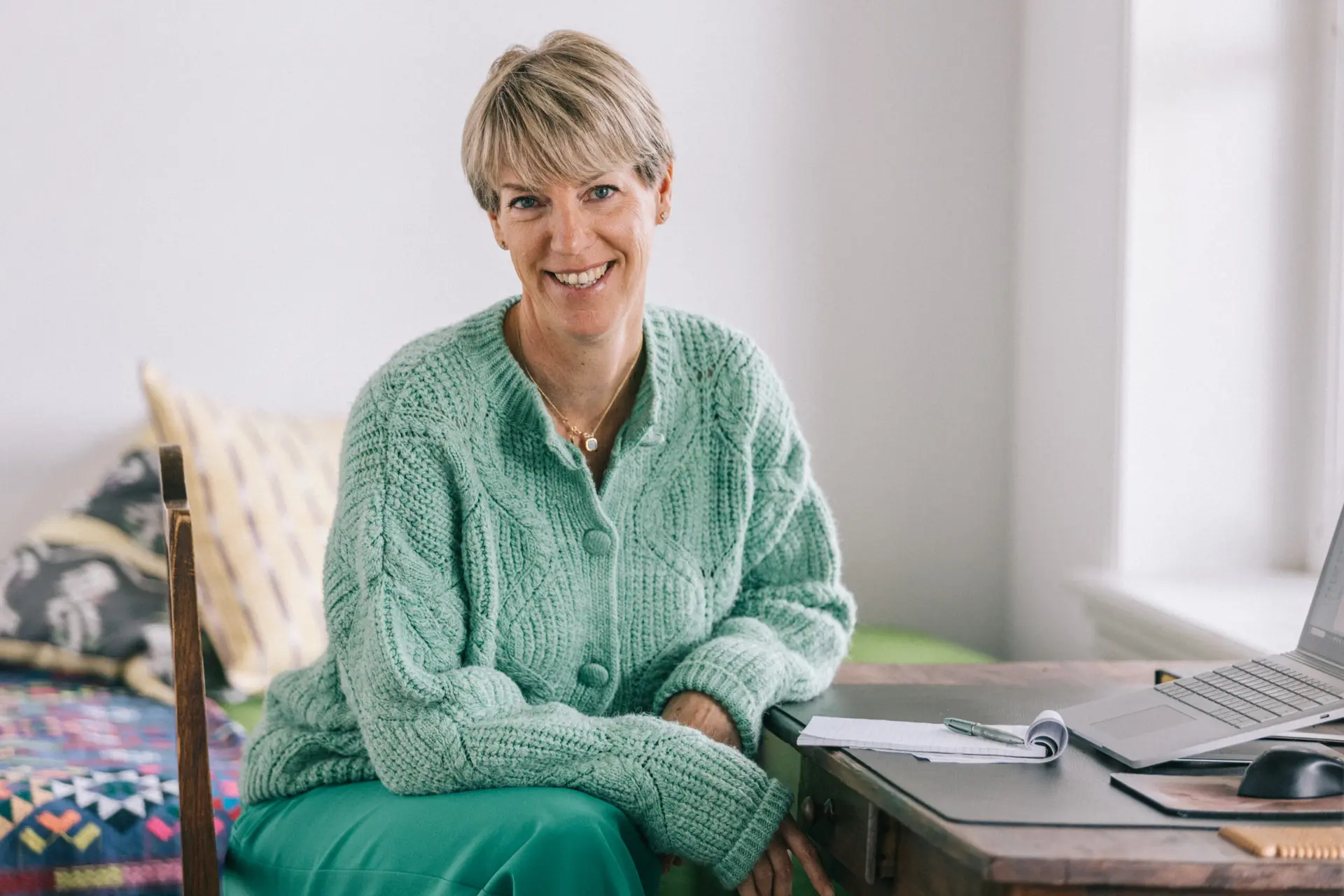 Kirsten Hermsen in een groene trui lacht in een lichte woonkamer