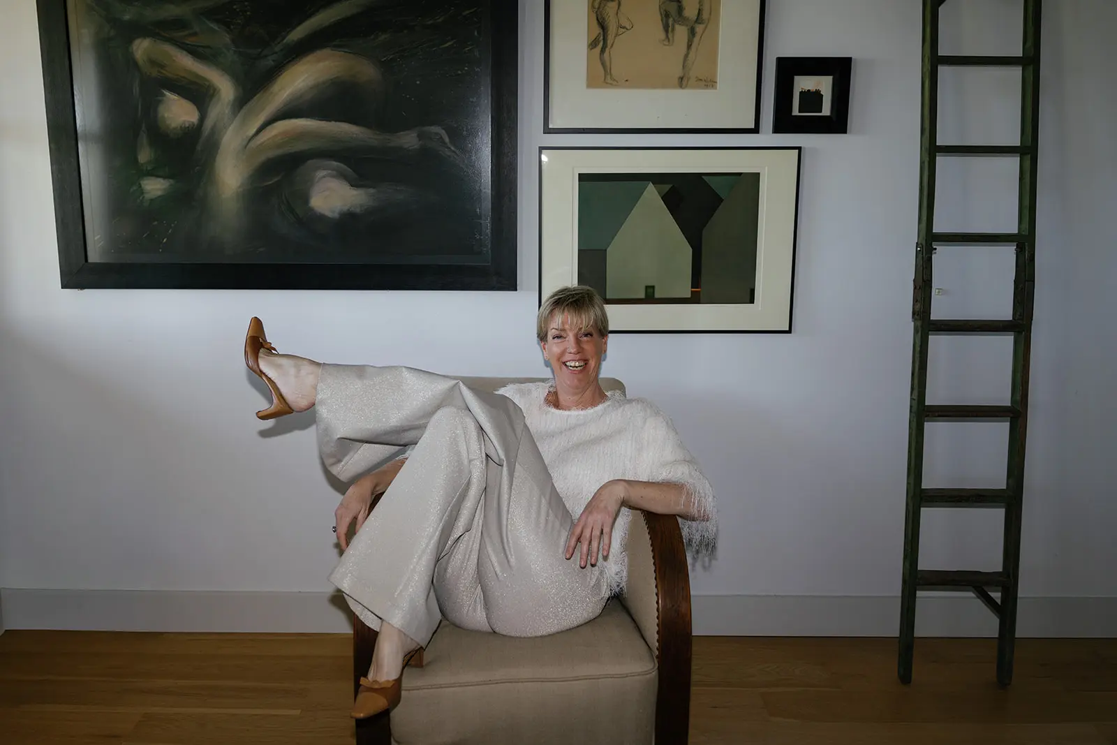 Kirsten Hermsen zit ontspannen in een stoel voor een wand met kunst