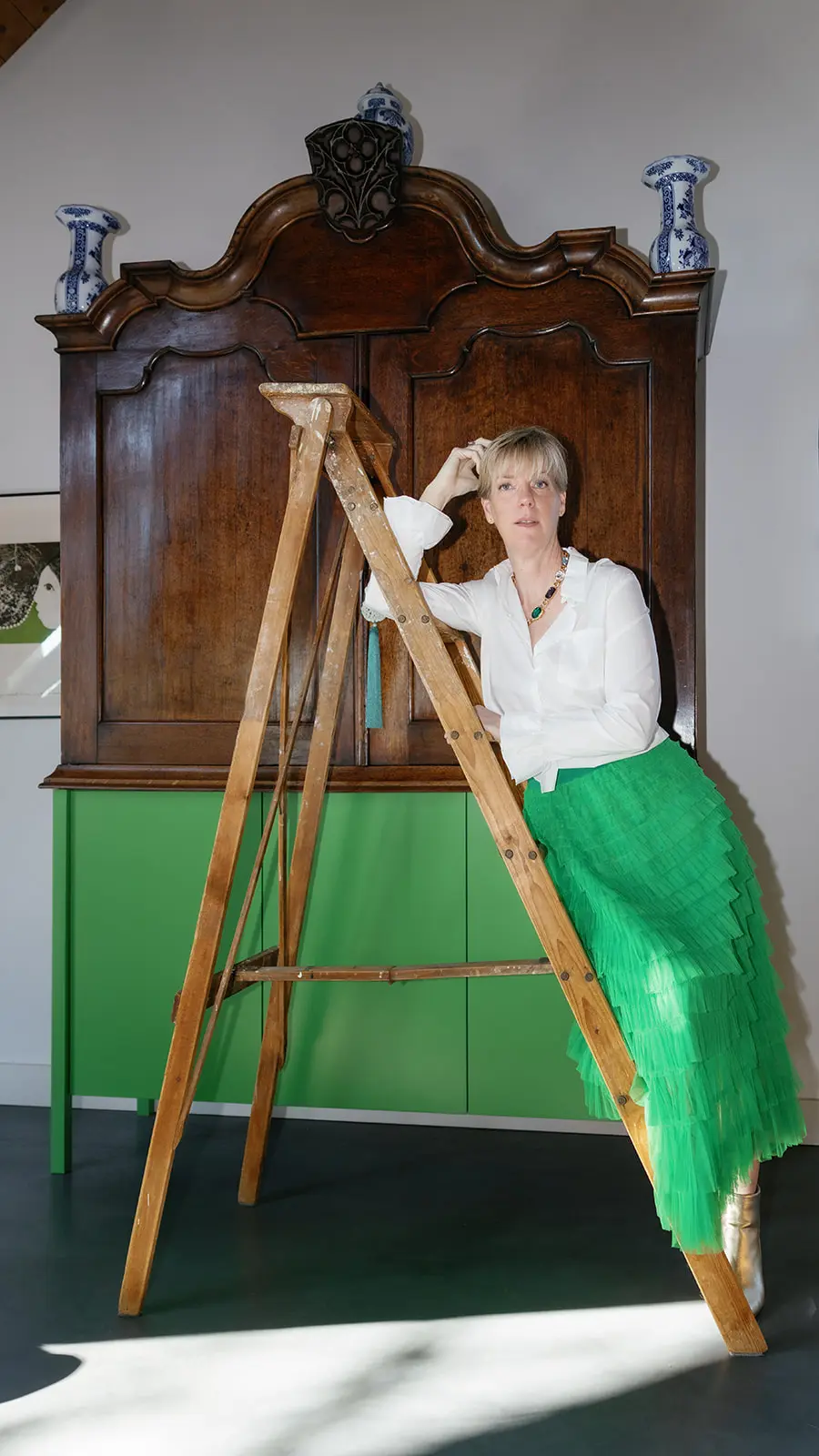 Kirsten Hermsen leunt tegen een ladder voor een antieke kast, in een groene rok