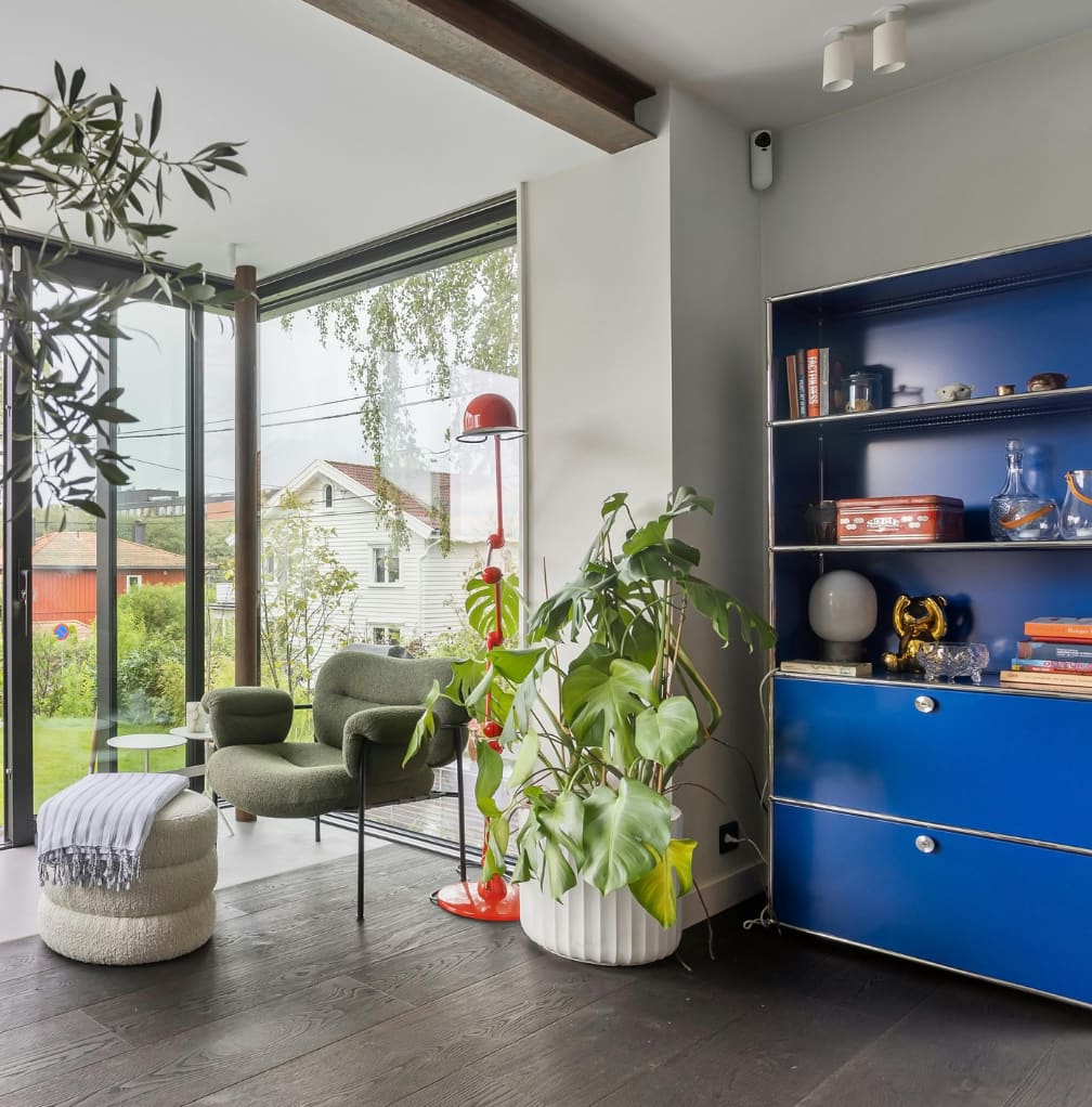 Zithoek met groene fauteuils, blauwe kast en veel planten bij een groot raam